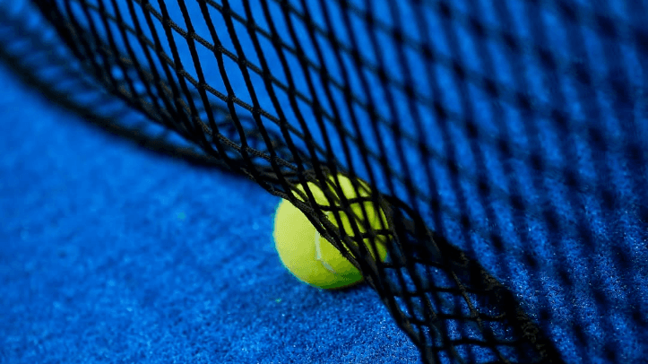 Pelota de pádel junto a la red sobre una pista azul